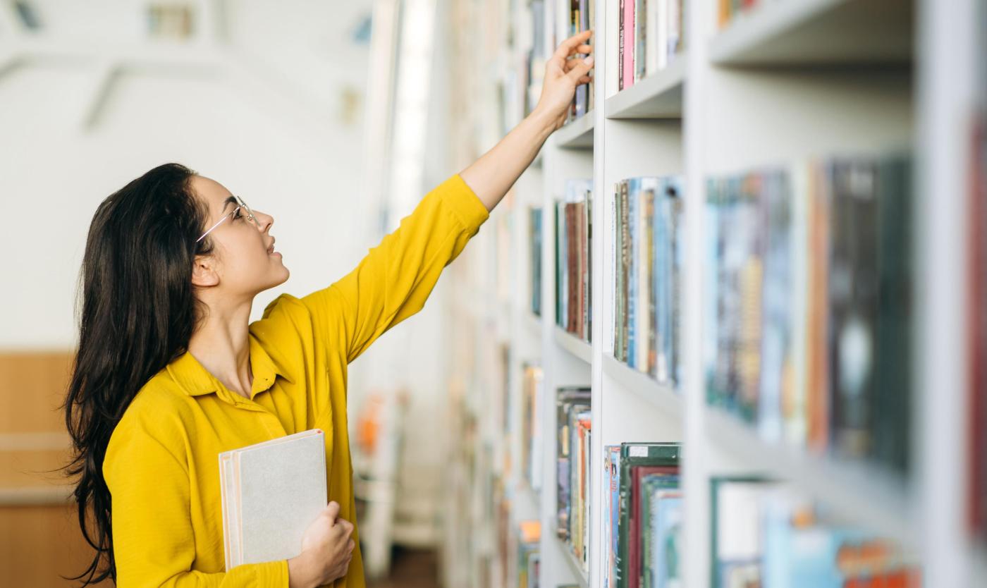 Vrouwelijke student op zoek naar een boek in een universiteitsbibliotheek