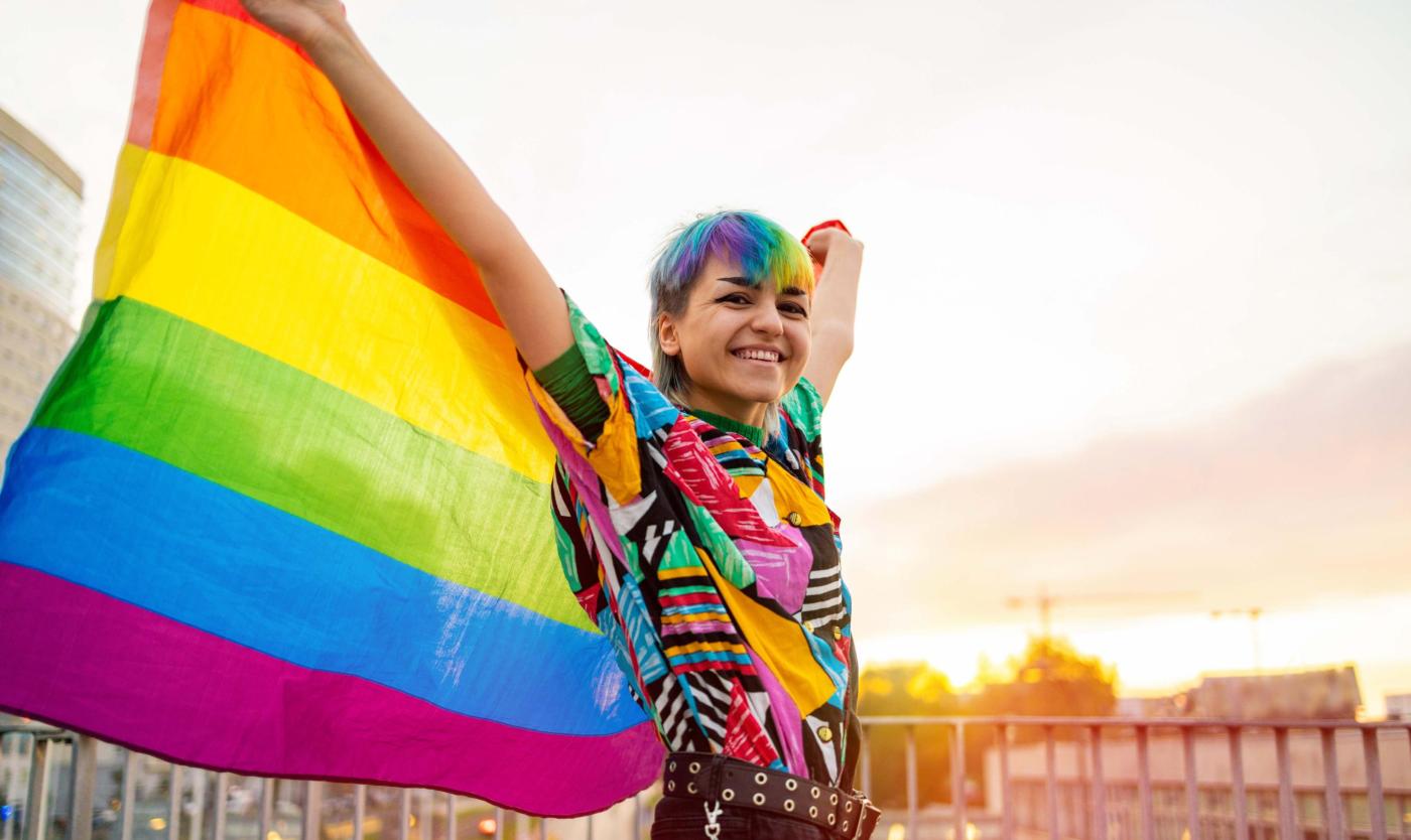2022_Portret van gelukkige gender neutraal persoon die regenboogvlag zwaait_S_1842595813