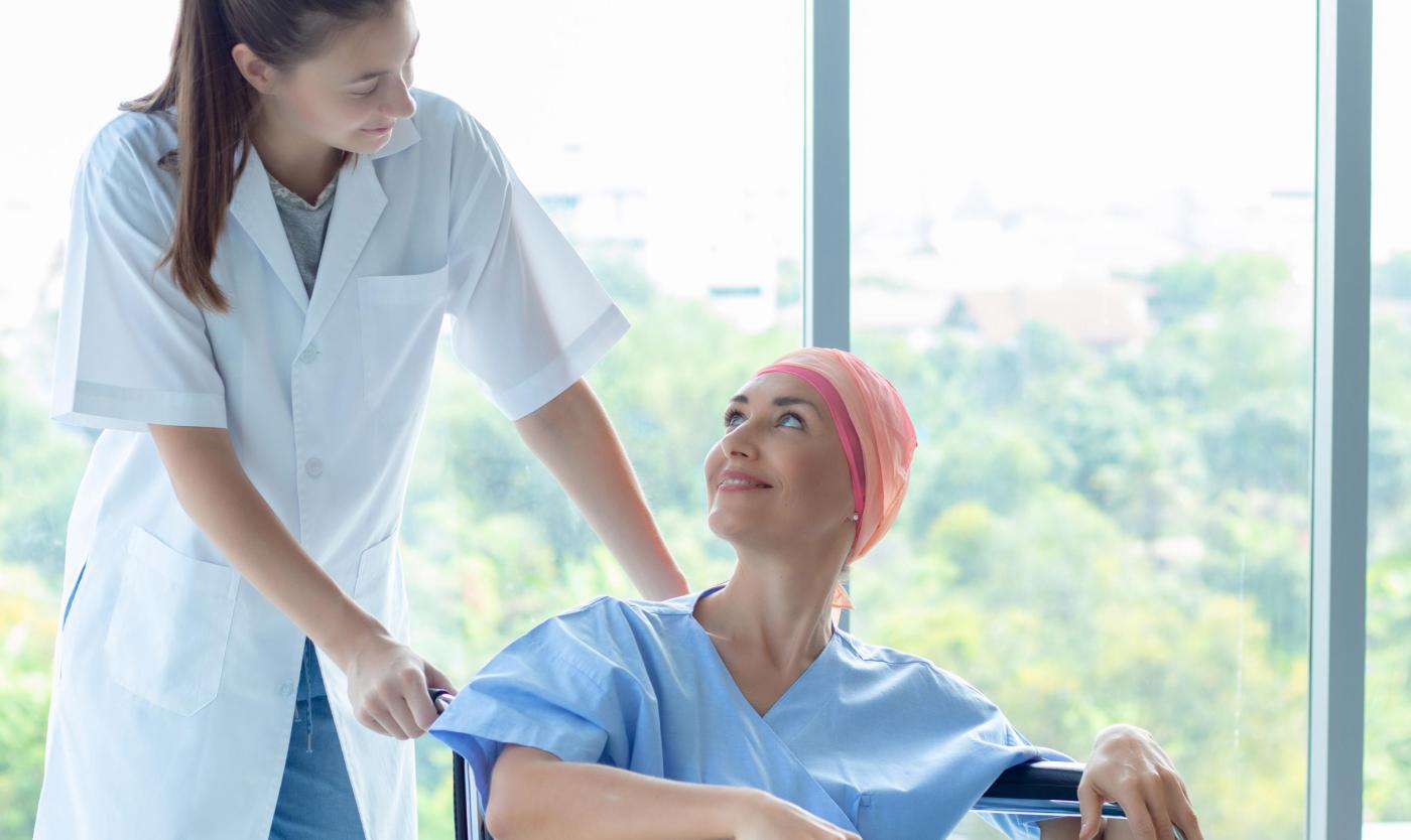 2022_Professionele verpleegster zorgt voor een patiënt_Blanke vrouw met hoofddoek veroorzaakt door chemotherapie voor kanker_Glimlachend en zittend in een rolstoel_S_1417469846