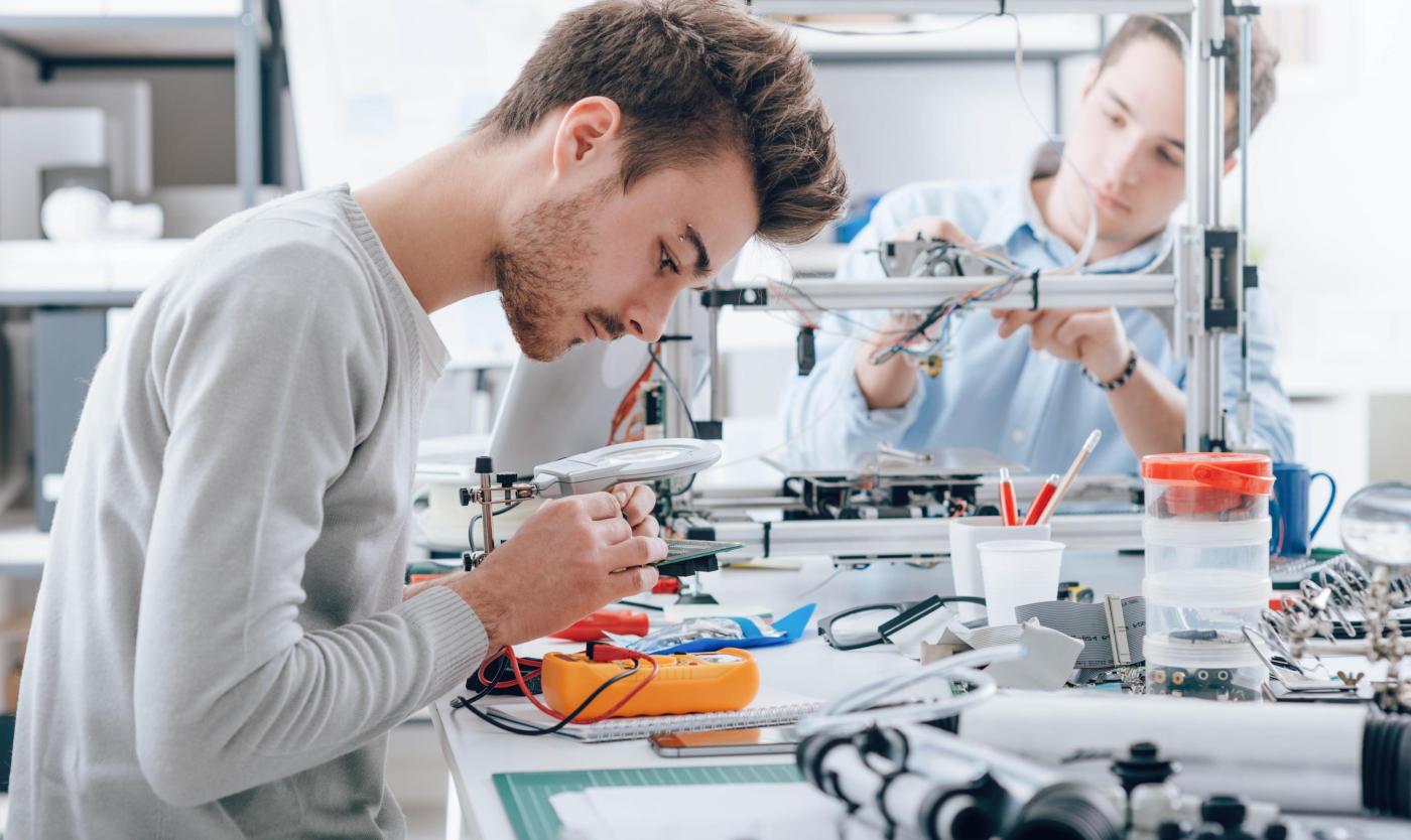 2022_Engineering studenten werken in het lab_Student gebruikt een spanning en stroom tester_Andere student op de achtergrond gebruikt een 3D-printer_FabLab_S_505534027