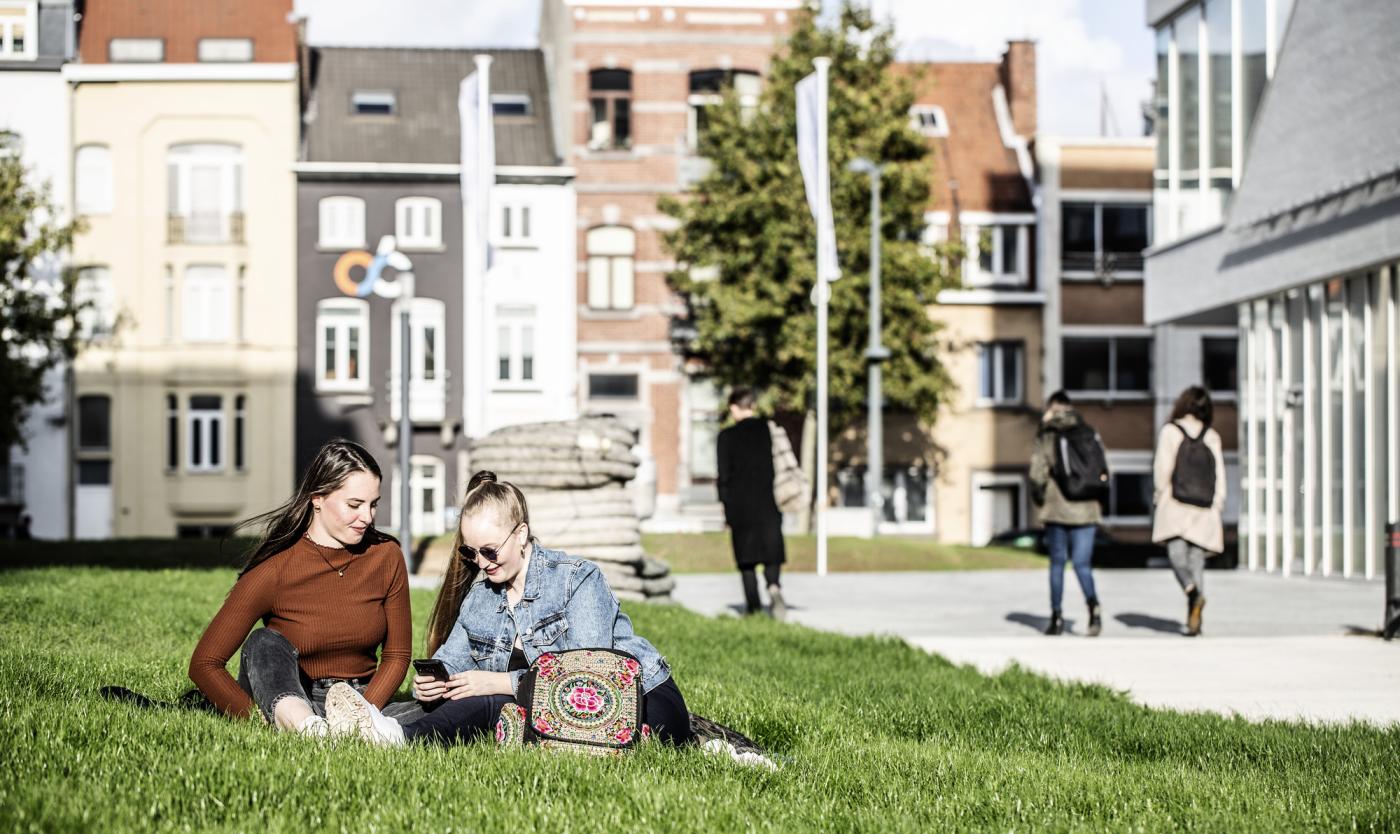 Studenten zitten op gras aan de IXY gebouwen op campus Etterbeek