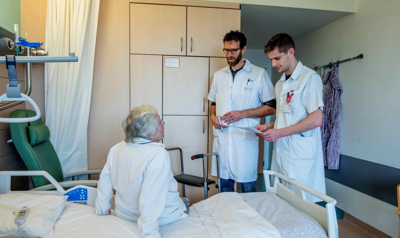 Artsen staan voor revalidatie aan het ziekenhuisbed van oudere patiënt
