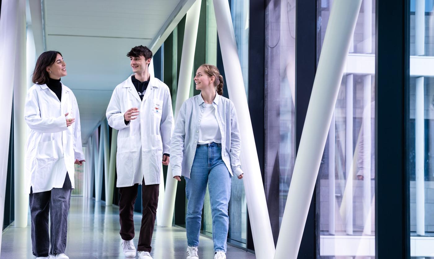 3 studenten wandelen in de passerelle tussen het UZ Brussel en de VUB Health Campus