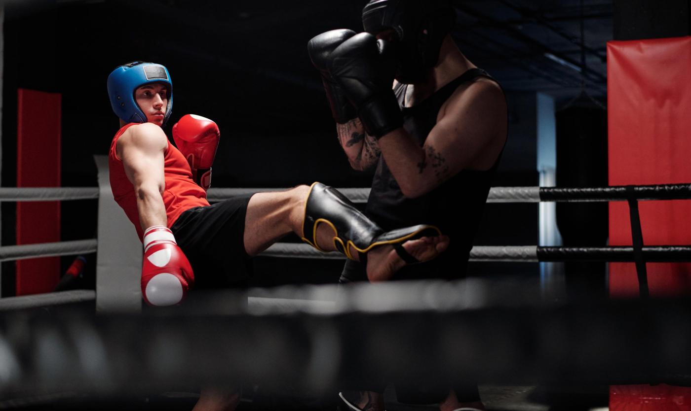 Young boxer in black sportswear defending from his rival giving low kick by leg in protective shinguard during sparring fight on boxing ring
