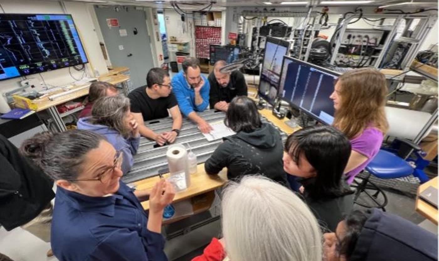 Low-Res_Team discussing preliminary results on the ship at the core table, image credit J Field-2.jpg