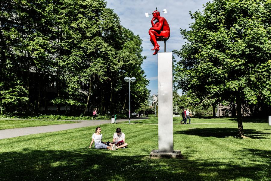 Studenten aan het praten op het grasveld met denker op Campus Etterbeek
