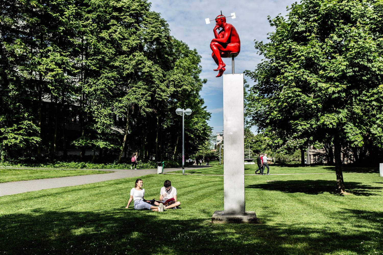 Studenten aan het praten op het grasveld met denker op Campus Etterbeek Studenten aan het praten op het grasveld met denker op Campus Etterbeek