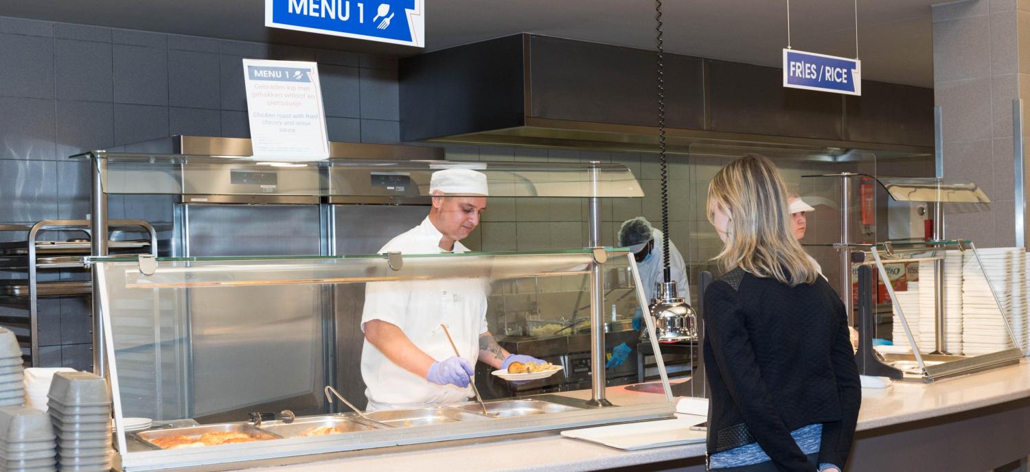 2022_Vrouw in resto neemt eten aan van keukenpersoneel_VUB Resto_Etterbeek_Banner 2022_Vrouw in resto neemt eten aan van keukenpersoneel_VUB Resto_Etterbeek_Banner