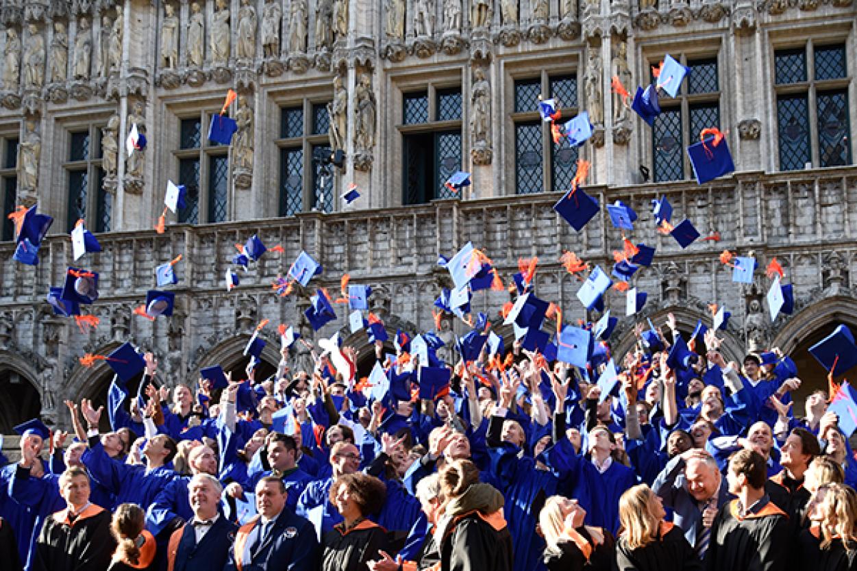 Afstudeerceremonie op de Grote Markt. Alumni gooien afstudeerhoedjes in de lucht