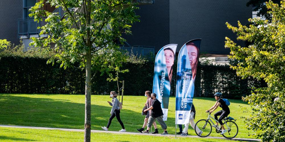 Studenten aan het wandelen en fietser op grasveld van Campus Etterbeek