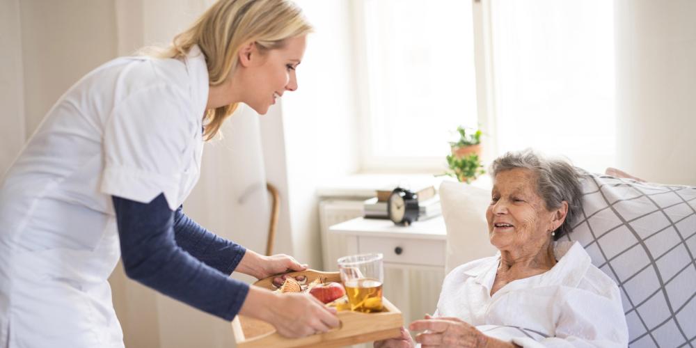 2022_Een gezondheidsbezoeker die ontbijt brengt naar een zieke oudere vrouw die thuis in bed ligt_Slaapkamer_S_1228707130