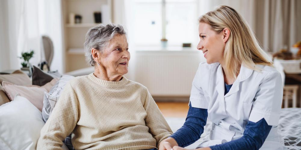 2022_Een gezondheidsbezoeker praat met een zieke senior vrouw die thuis op bed zit_Woonkamer_S_1290675772.jpg