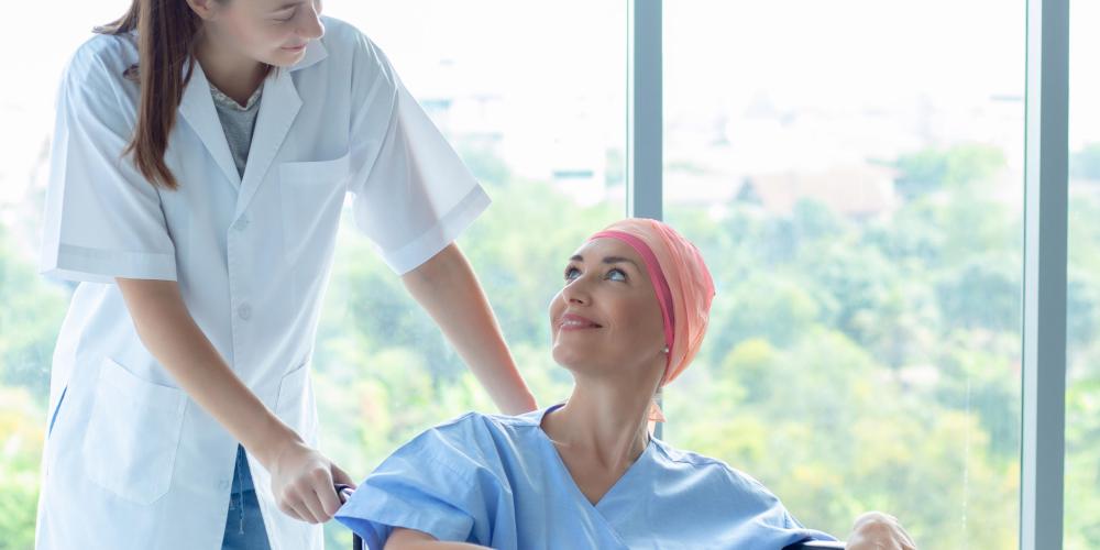 2022_Professionele verpleegster zorgt voor een patiënt_Blanke vrouw met hoofddoek veroorzaakt door chemotherapie voor kanker_Glimlachend en zittend in een rolstoel_S_1417469846