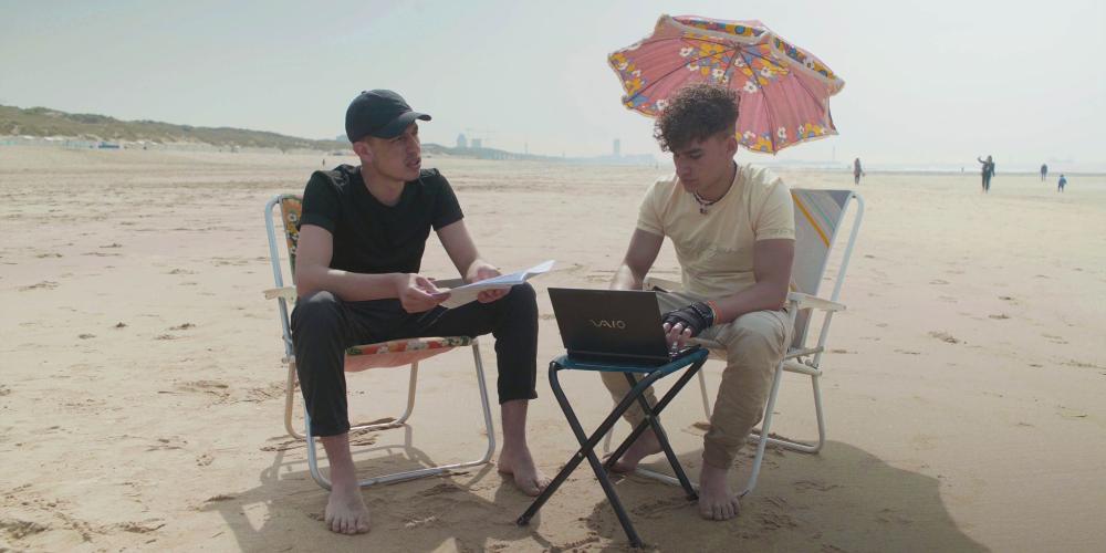 Twee jongens op zitten op stoelen aan het strand. Stilbeeld uit een film overAsiel en kinderrechten
