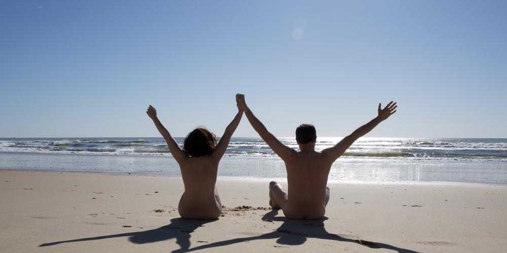 Nudisten zitten op strand Een koppel nudisten zitten op het strand met hun armen omhoog