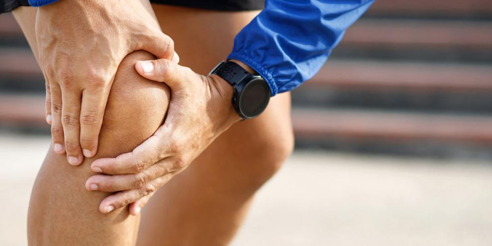 Iemand grijpt naar een pijnlijke knie Iemand grijpt naar een pijnlijke knie