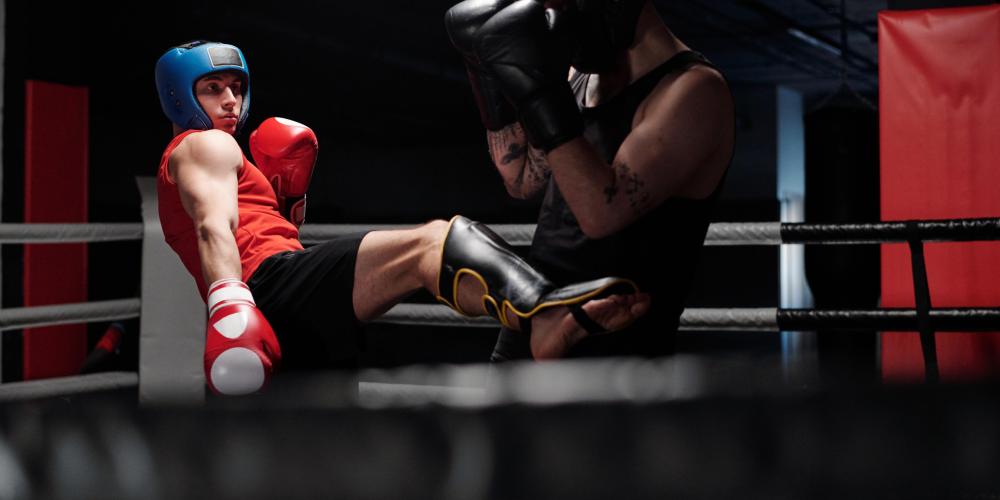 Young boxer in black sportswear defending from his rival giving low kick by leg in protective shinguard during sparring fight on boxing ring